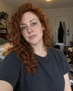 Example phone photo: a selfie of a freckled woman with long red curls in a grey T-shirt in a cluttered room