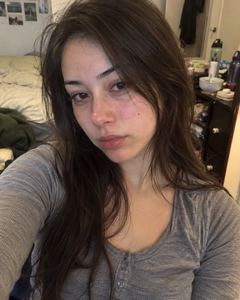Example phone photo: a selfie of a young woman with long dark hair in a grey top in her bedroom